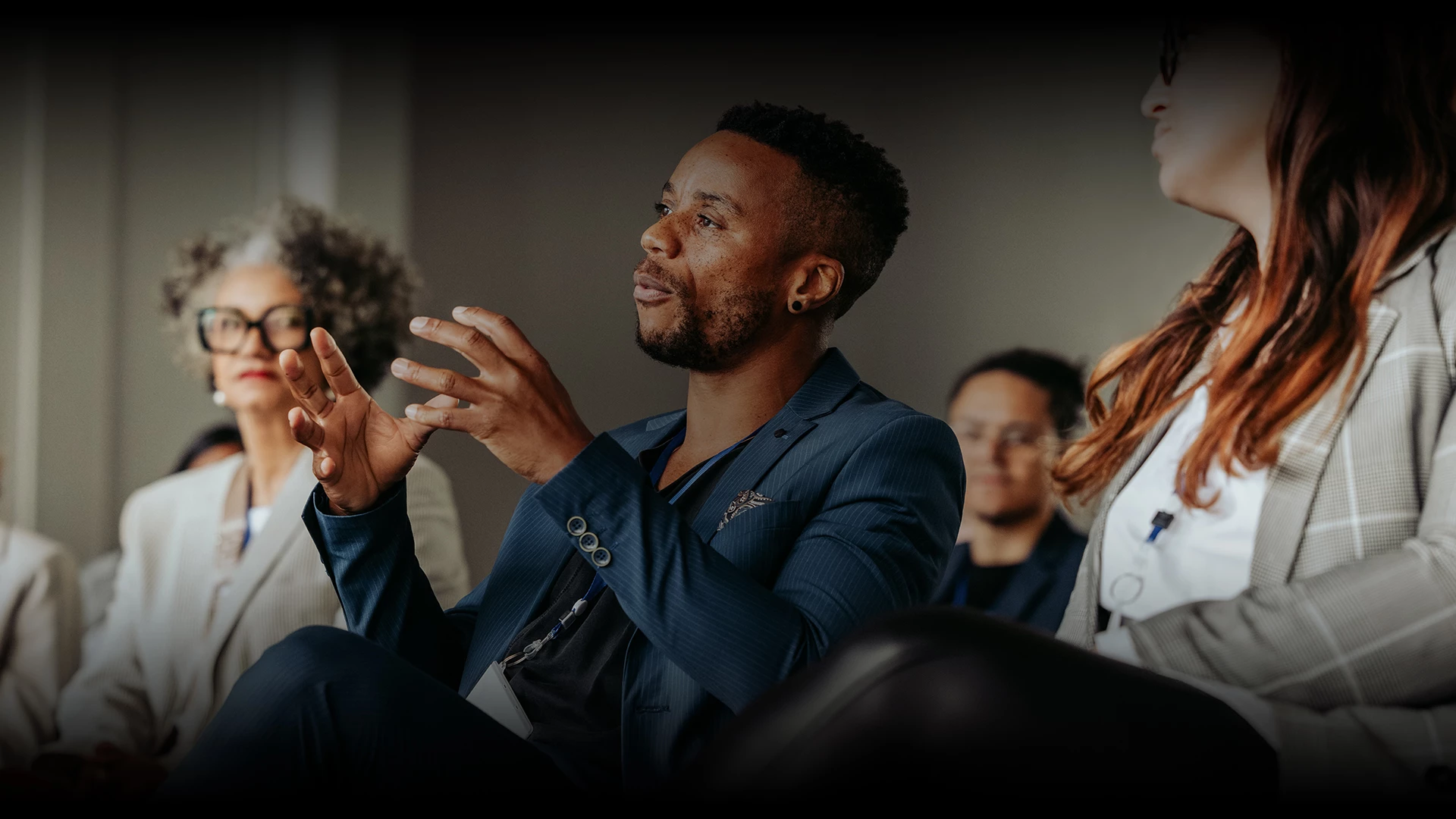 a man in a suit sitting in a room with other people