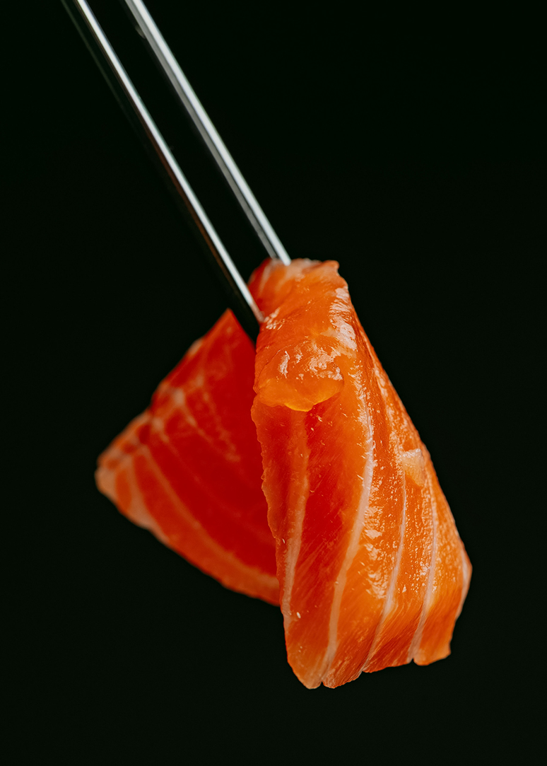 a piece of raw salmon with chopsticks