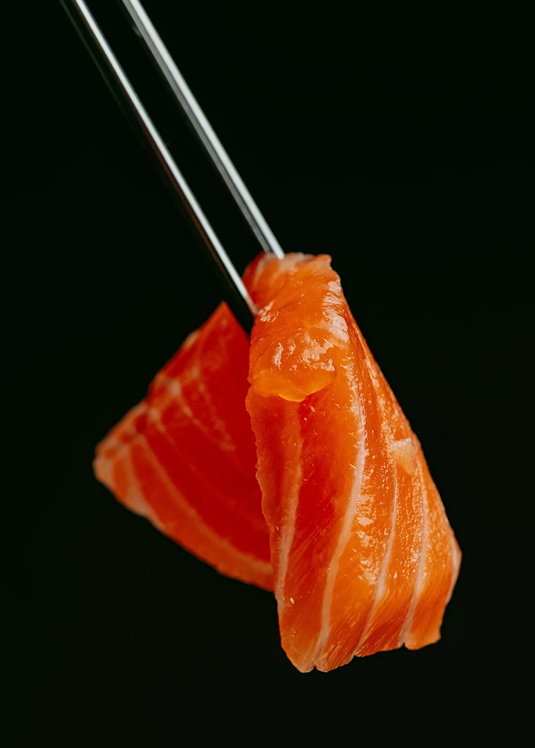 a piece of raw salmon with chopsticks