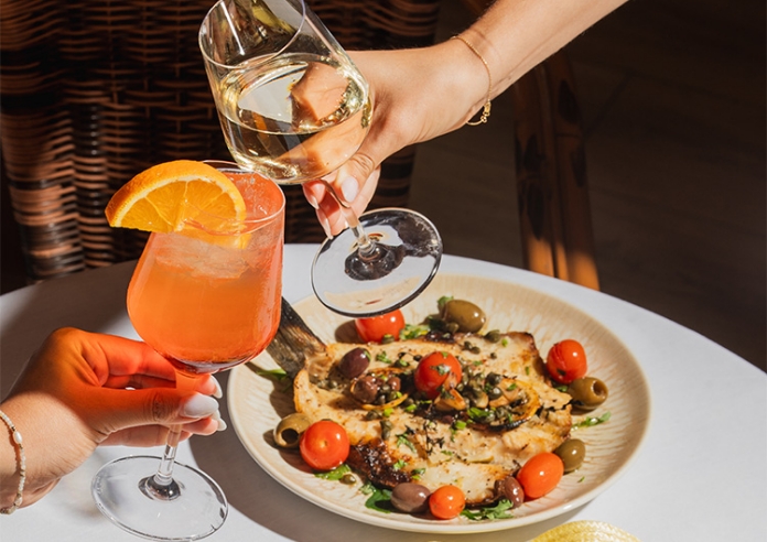 a person holding wine glasses over a plate of food