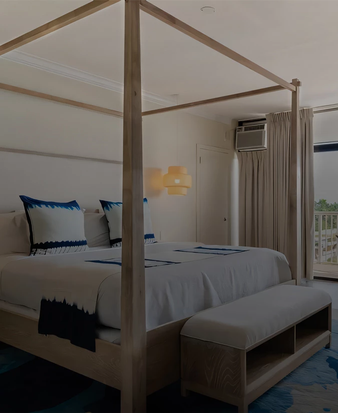 A neatly made bed with white and blue linens in a room with a window and balcony.