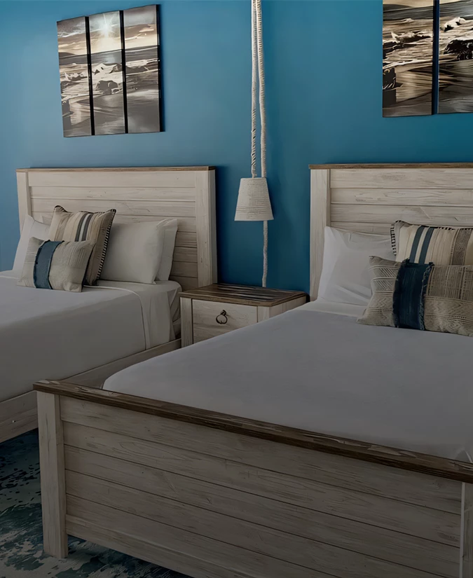 A hotel room with two beds, wooden furniture, and blue walls adorned with artwork.