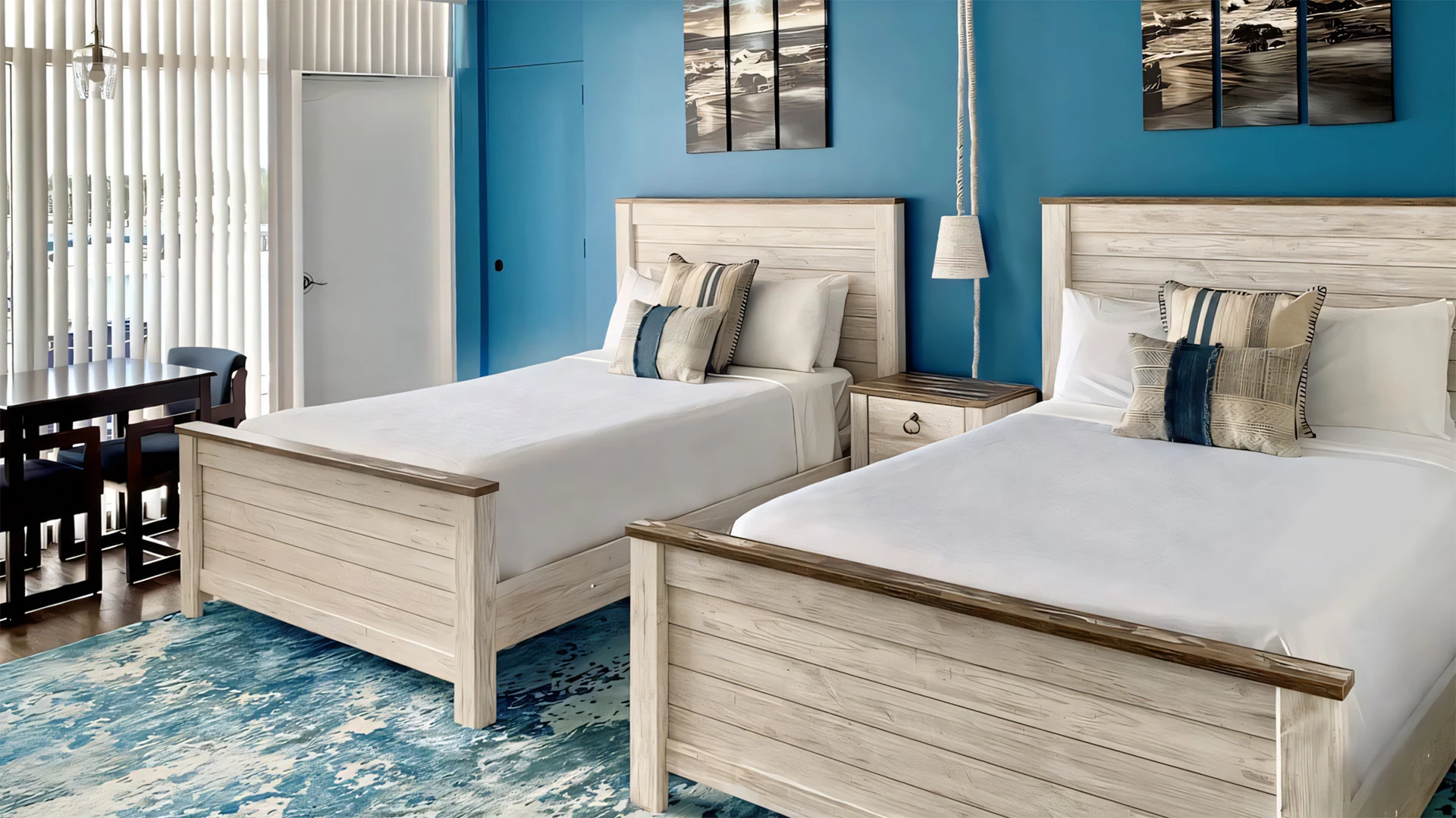 A hotel room with two twin beds, a blue accent wall, and a window with blinds.