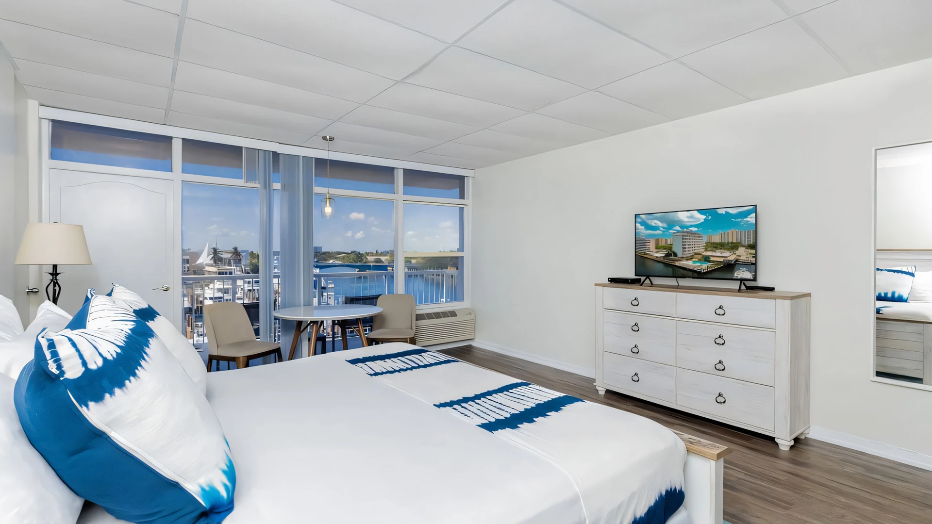 A hotel room with a bed, TV, dresser, and table by the window.