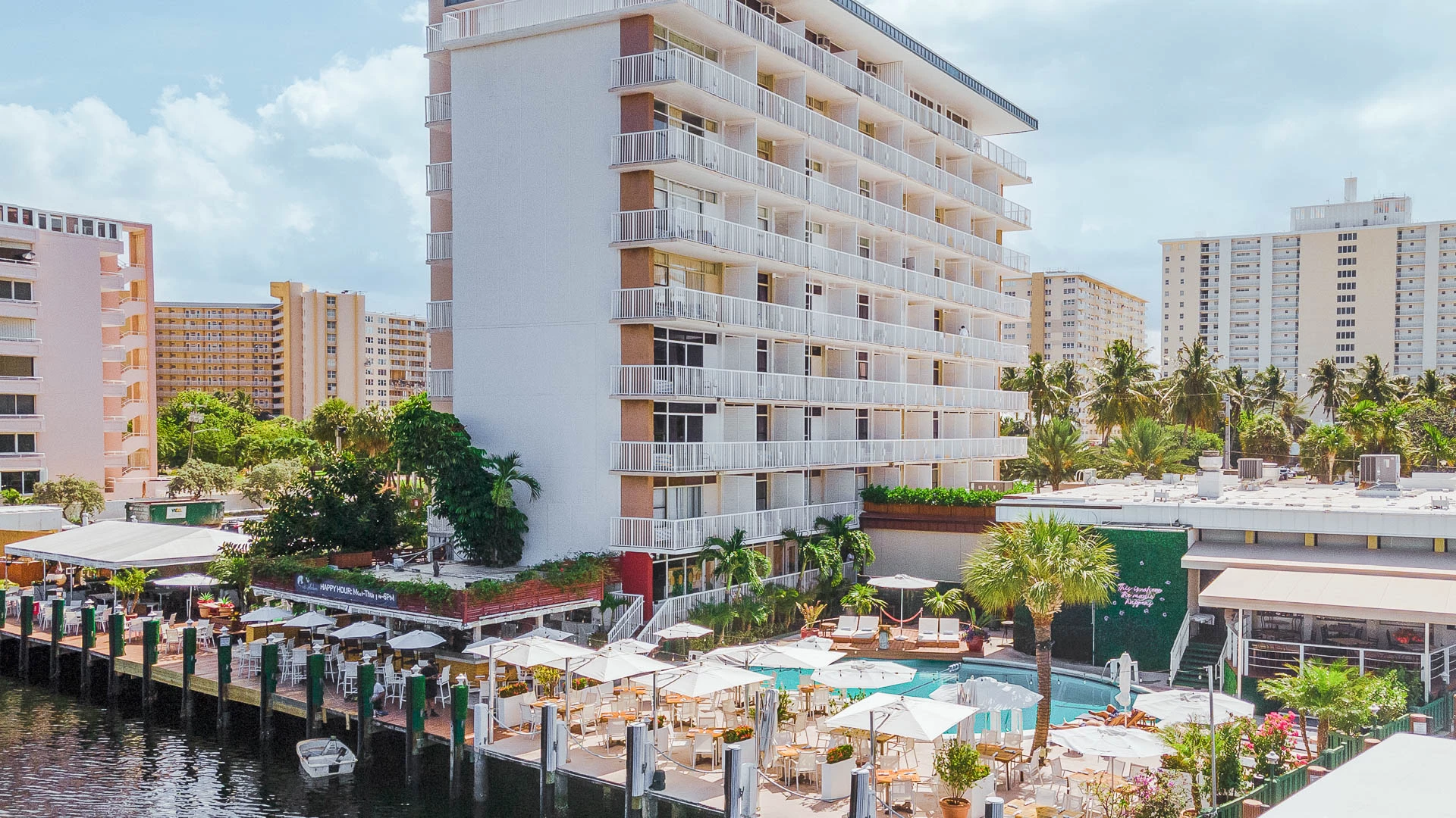 A large white building with balconies overlooking a pool and water