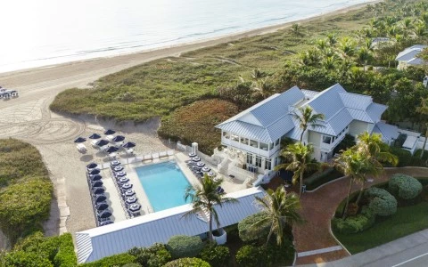 a building with a pool and palm trees on the beach