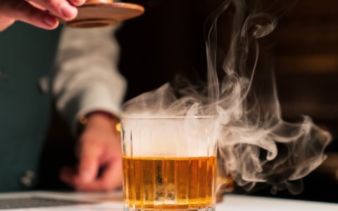 a person pouring a drink into a glass with smoke