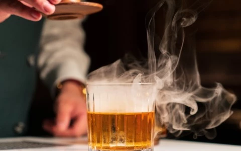 a person pouring a drink into a glass with smoke