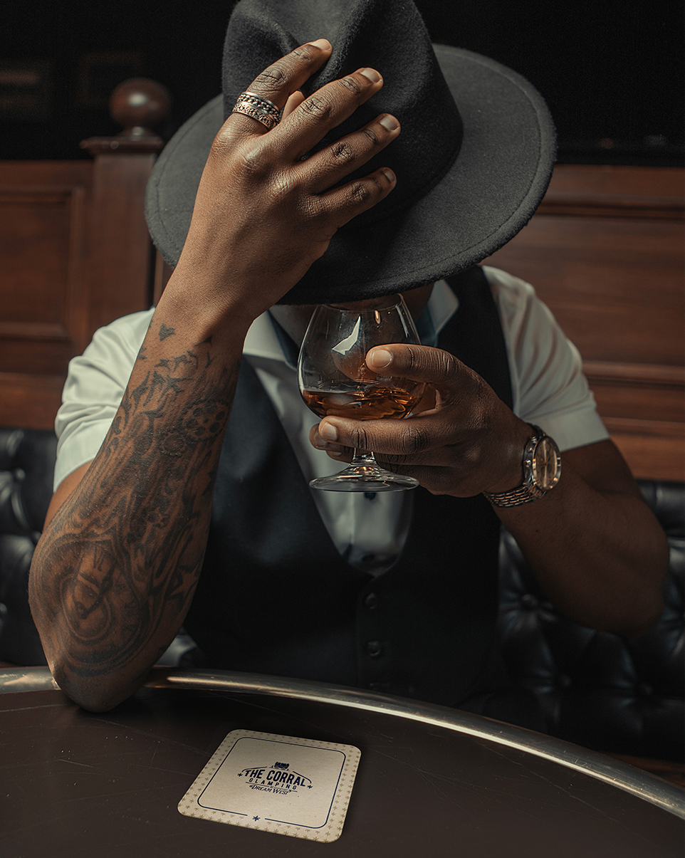 a man with a hat covering his face with a glass of alcohol