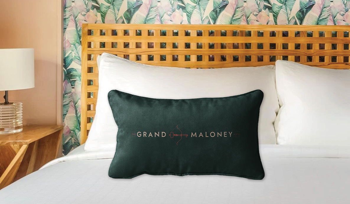 a dark green pillow on a bed with The Grand Maloney Hotel Logo