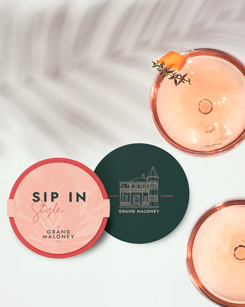 two drinks next to two coasters with Grand Maloney Hotel Branding & logo on them