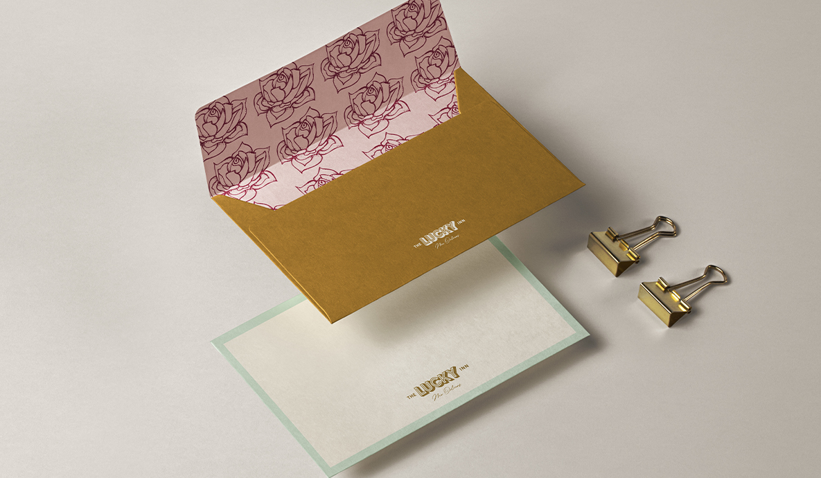 a gold envelope with a pink and white flower pattern and the Lucky Inn logo on it