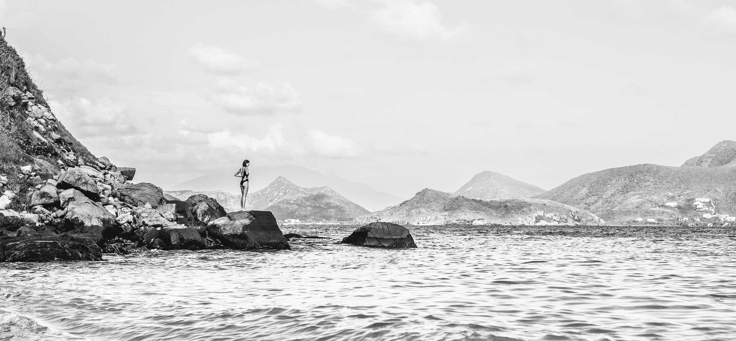 a woman standing on rocks in the water with mountains in the background