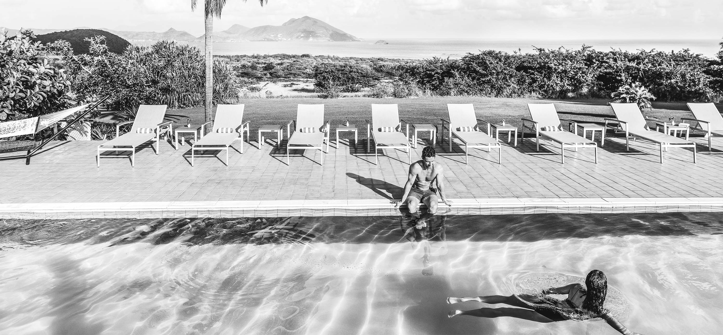 a man sitting on the edge of a pool and a girl swimming in the pool