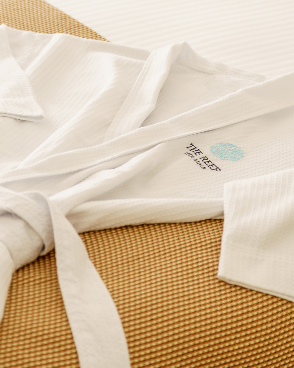 a white robe on a bed with the Reef logo on it