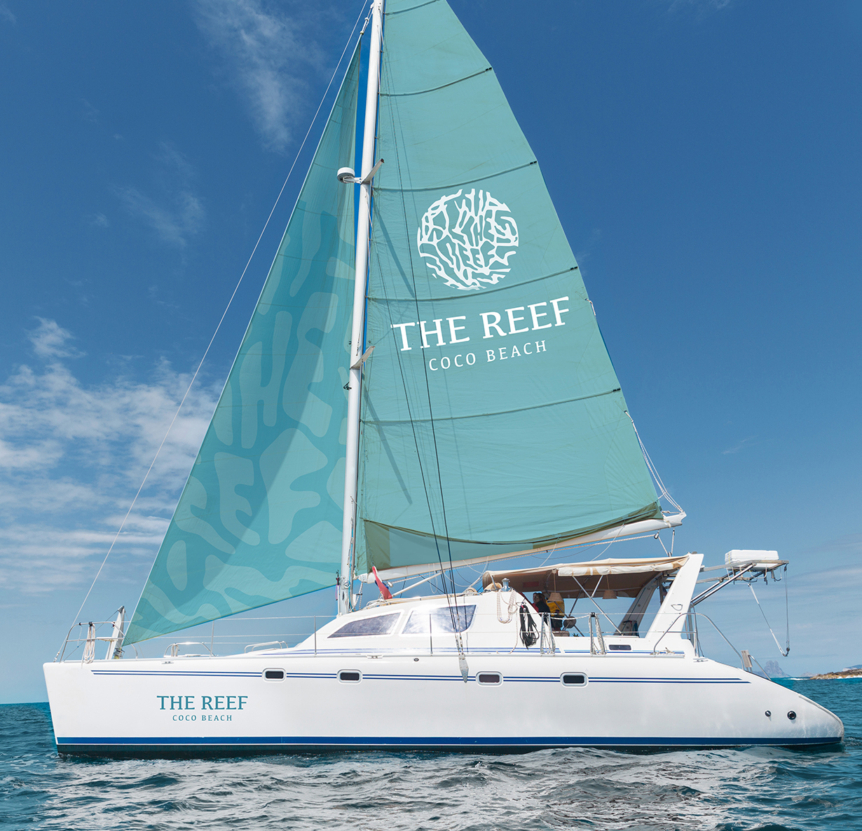 a white boat with blue sail that has The Reef logo on it