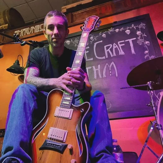 Andy Moses sitting on a stage holding a guitar