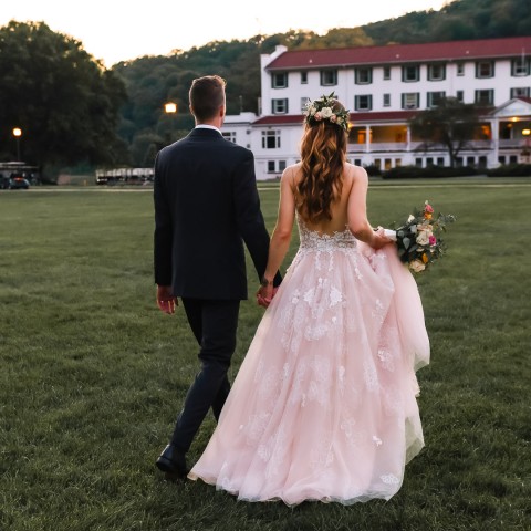 a man and woman holding hands and walking on grass