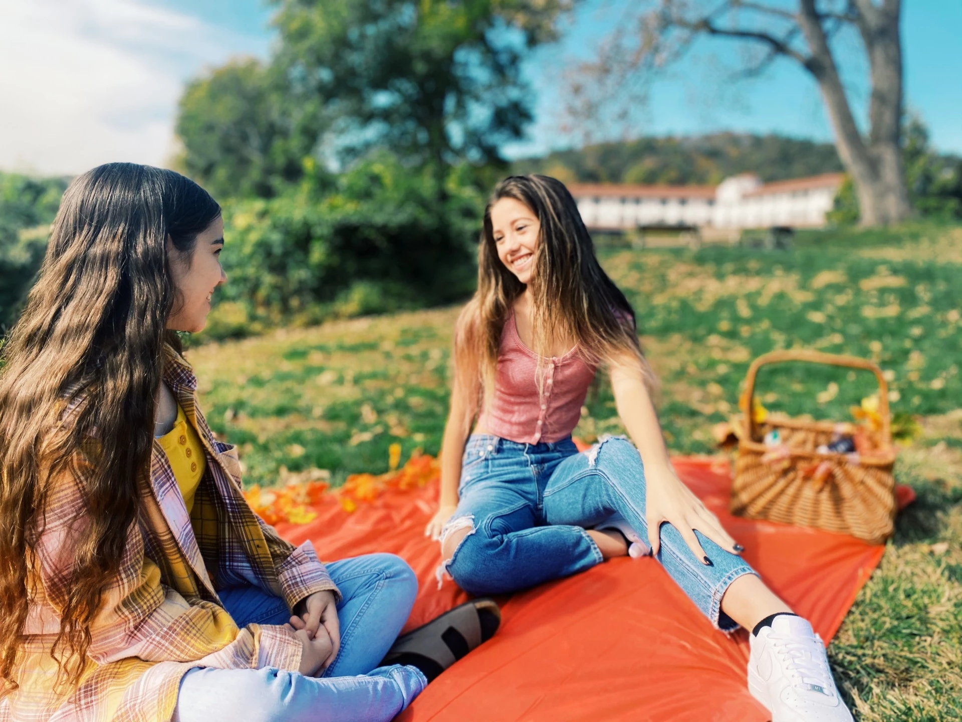 two girls sitting on a blanket in a park