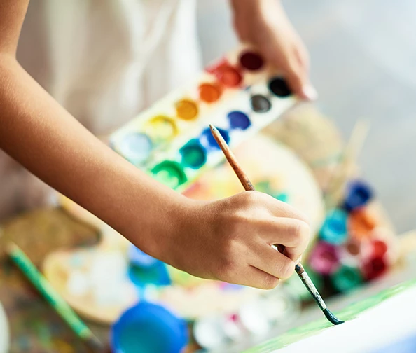 a hand holding a paintbrush and a palette of paint