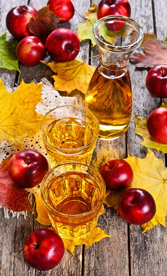 a group of glasses of liquid and apples on a table