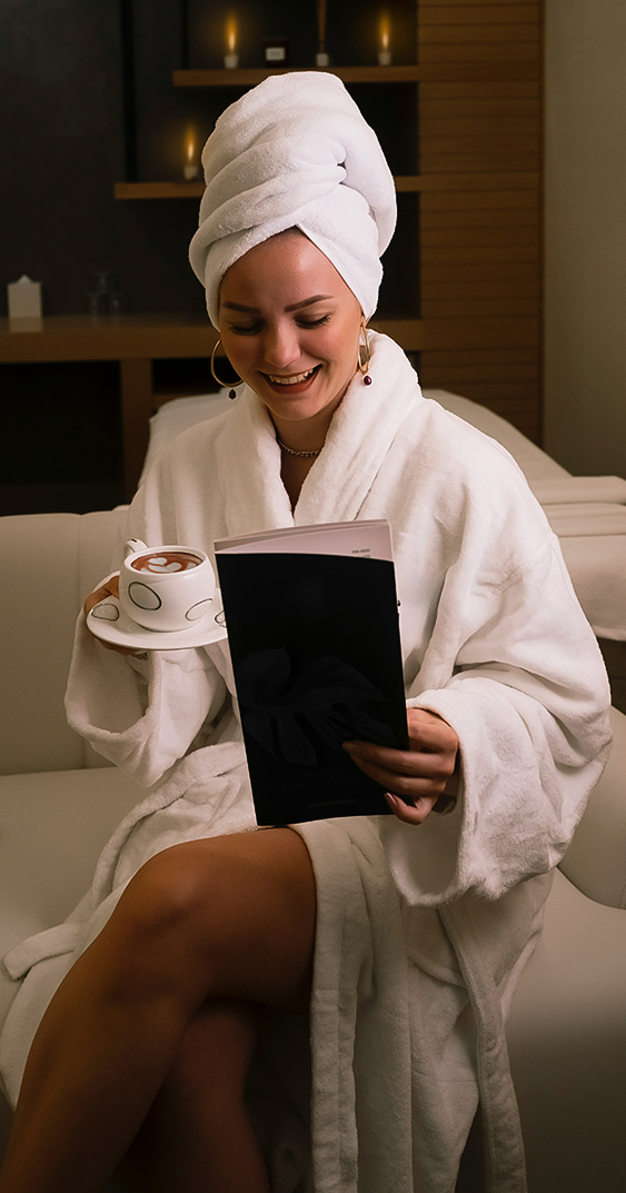 a woman in a white robe and towel holding a book and a cup of coffee