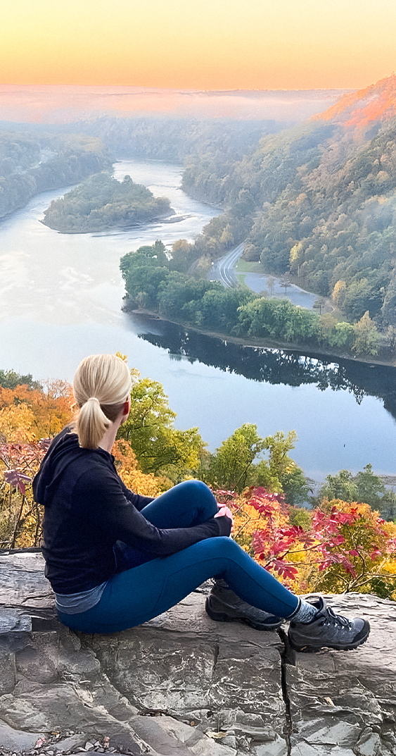 a woman sitting on a cliff overlooking a river