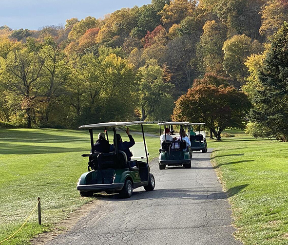 a group of people driving golf carts on a road with trees in the background