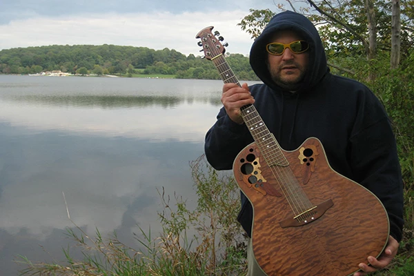 a man holding a guitar by a lake - Ziggy