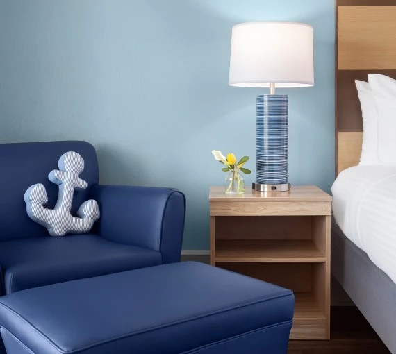 a blue chair with a white and blue anchor pillow next to a lamp
