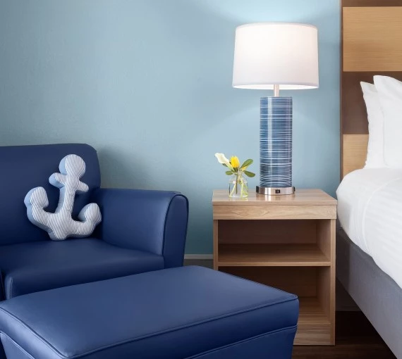 a blue chair with a white anchor pillow and a lamp on a table