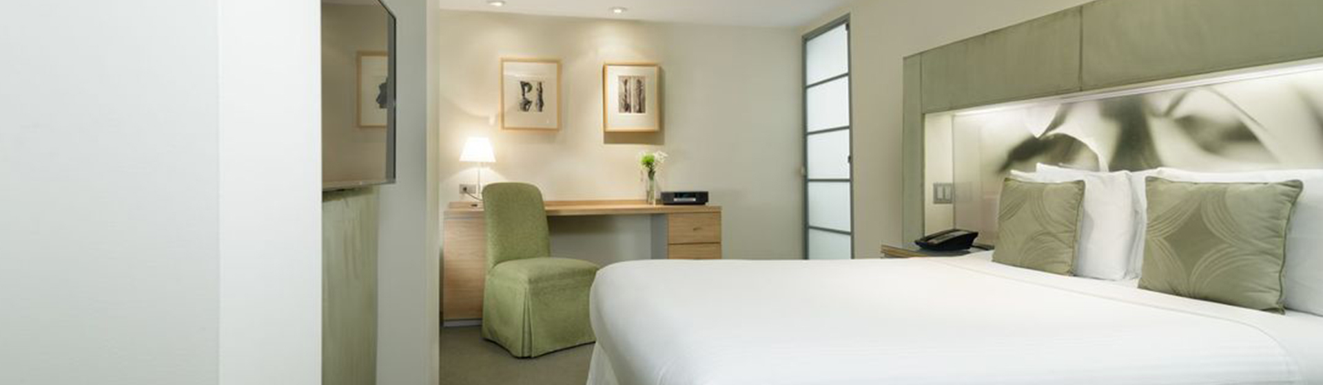 A neatly arranged hotel room with a large bed, desk, chair, and artwork on the walls.
