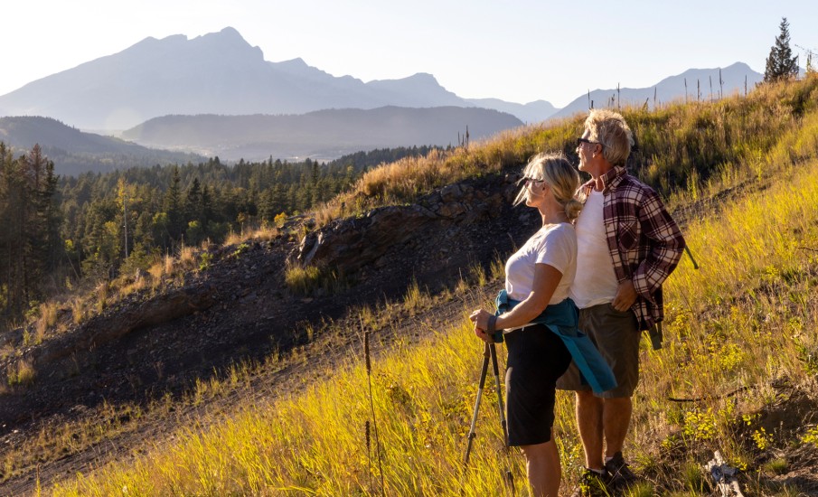 a man and woman kissing on a hill with trees and mountains in the background