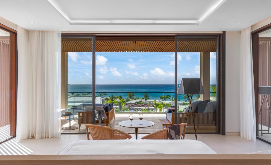 Two wine glasses on a table in front of sliding glass doors with views of the Caribbean at Silversands Grand Anse.