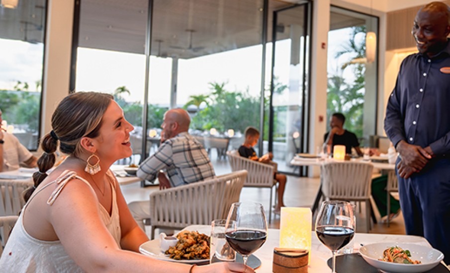a woman smiling at a table with food and wine glasses