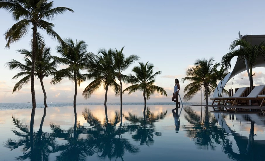 a woman sitting on a bench in front of a pool with palm trees