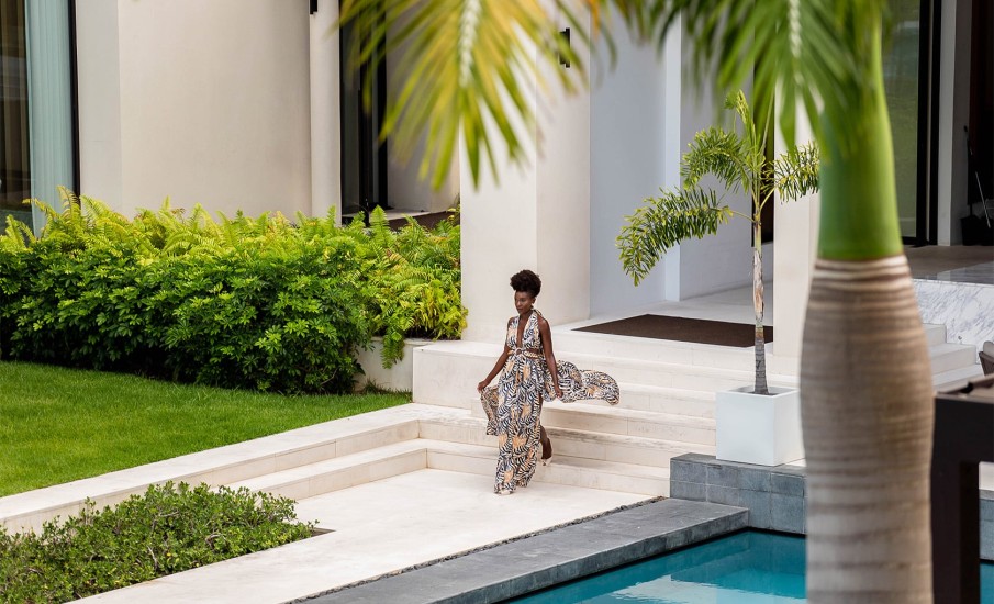 A woman wearing a flowing summer dress walking along a white stone patio next to a pool at Silversands Grand Anse Resort in Grenada.