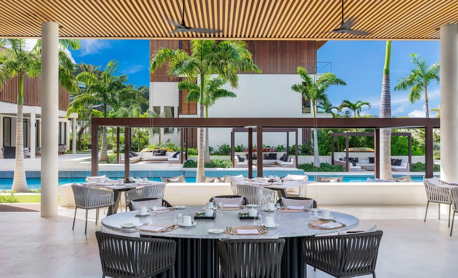 Dining tables in an open-air setting next to the pool and palm trees at Silversands Grand Anse in Grenada.