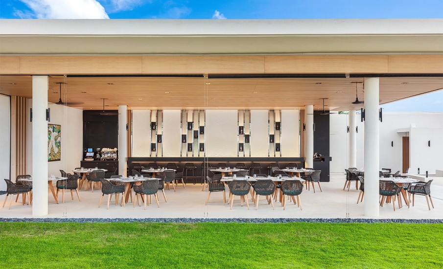 Exterior view of the open air dining area at Grenadian Grill in Grand Anse Beach showing a lush grass lawn in front of a row of dining tables.