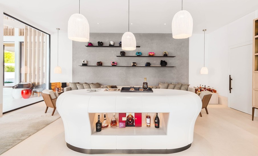 A white bar table with a built in shelf displaying bottles of premium rum, whiskey and cognac at Puro bar in Grand Anse.