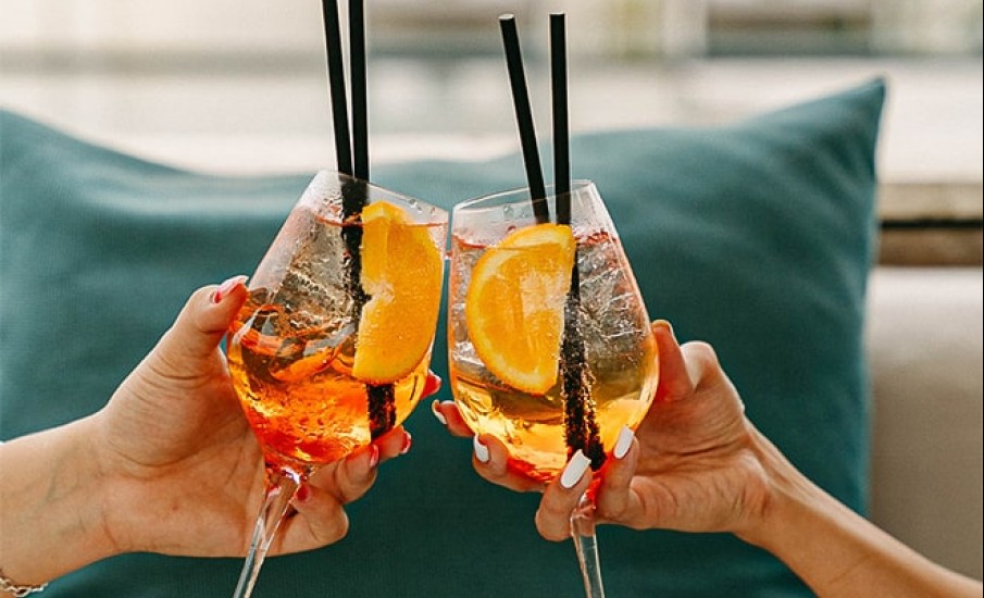 A close-up of two people toasting craft cocktails that are granished with orange slices at Puro rum bar at Silversands Grand Anse.