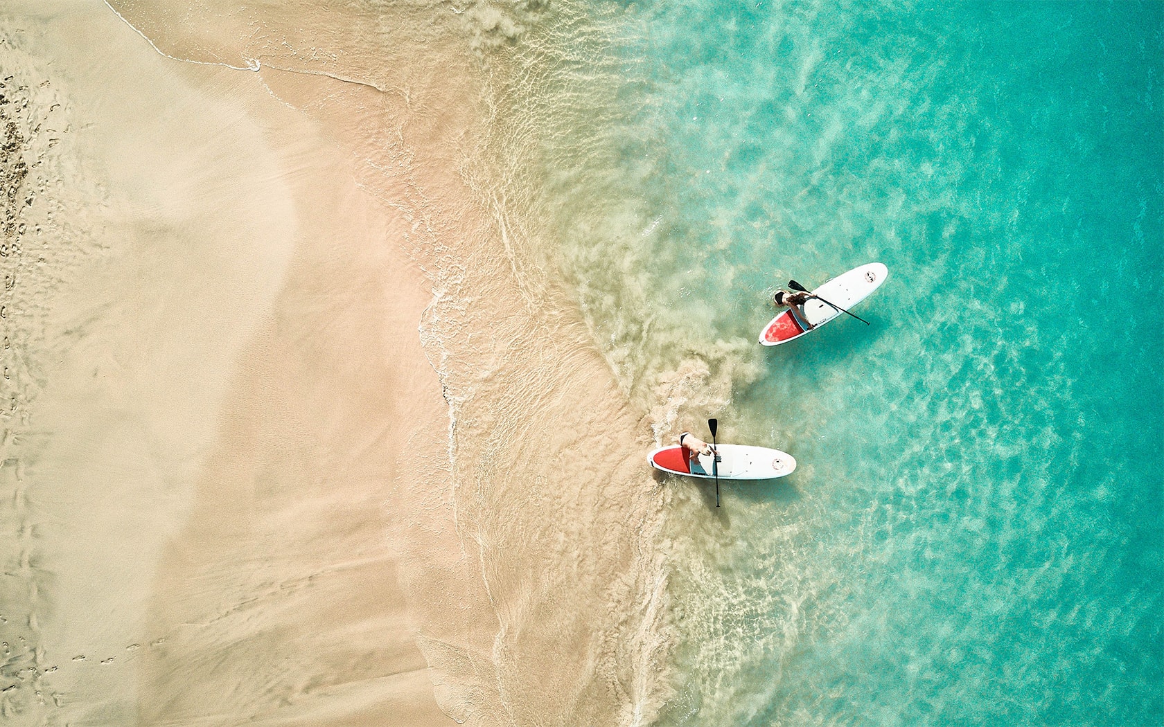 a couple of people stand on a surfboard in the ocean