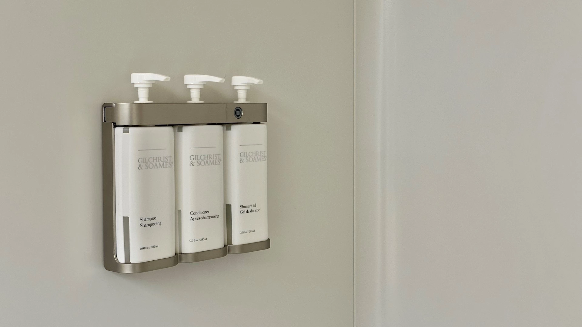 Three white bottles of shampoo, conditioner, and shower gel mounted on a wall.