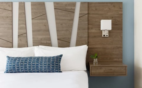 A close-up of a bed with a wooden headboard, white bedding, and a blue accent pillow.
