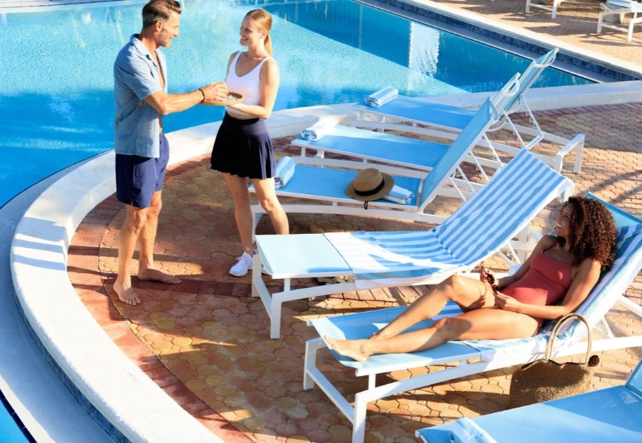 Three people are gathered by the pool, with two lounge chairs and a hat visible.