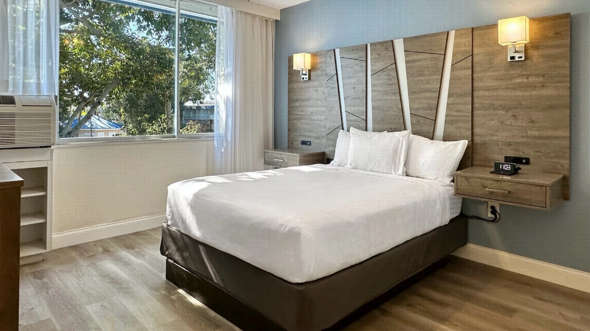 A hotel room with a large bed, window, and modern lamps