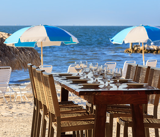 a table with wine glasses and plates on a beach