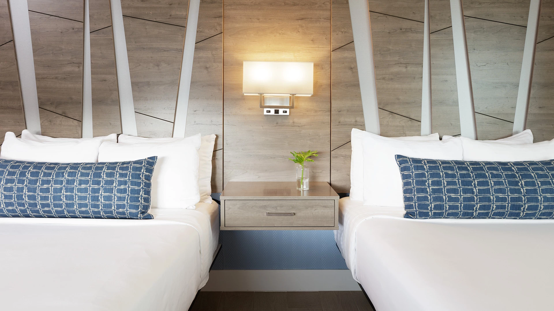 A hotel room with two beds, a nightstand, and a lamp.