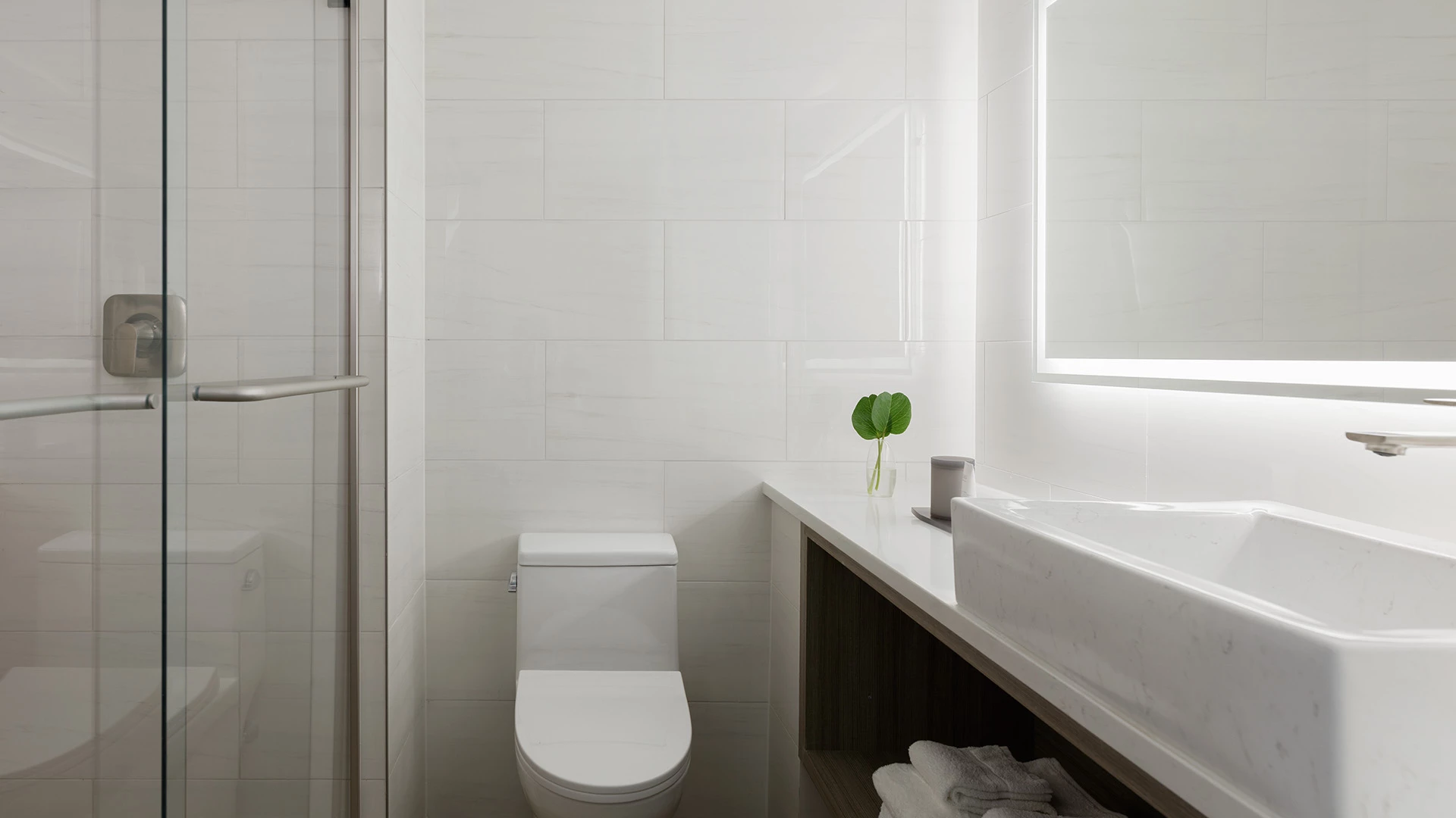 A modern bathroom with white tile, a glass shower door, and a single sink.