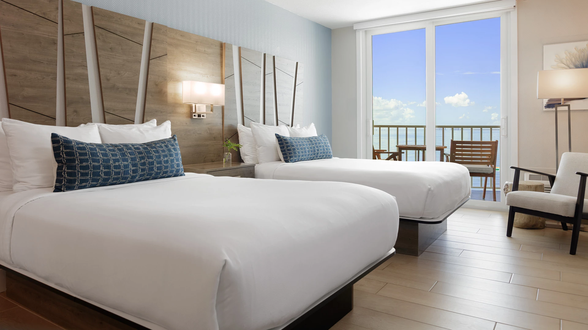 A hotel room with two queen beds, a wooden headboard, and a balcony with an ocean view.
